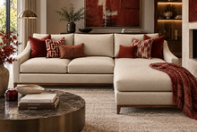 Load image into Gallery viewer, Bespoke cream linen corner sofa with chaise, styled with cadmium and brick red patterned scatter cushions in a luxury modern interior.

